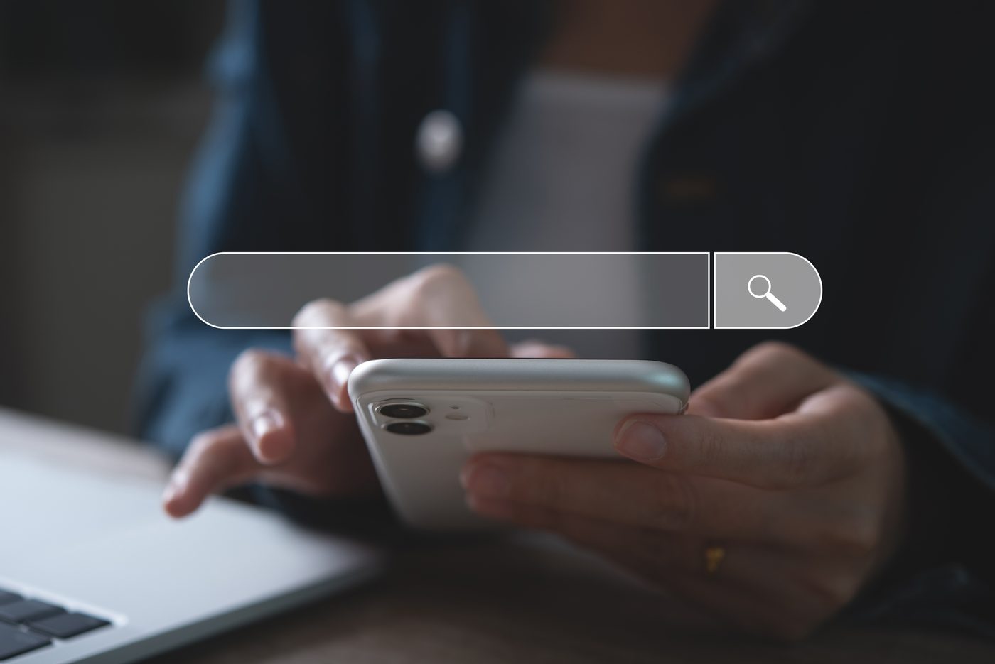 Person searching on a phone beside a laptop